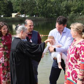 Taufe am Badesee Schortens: Pastorin tauft ein Baby, das auf dem Arm gehalten wird